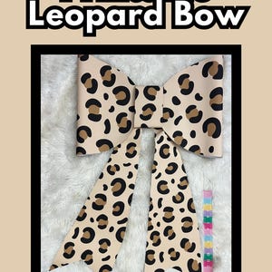 Puede incluir: Un lazo grande imprimible con fondo beige y un patrón de leopardo en negro y marrón. El lazo incluye dos cintas largas y puntiagudas, y se muestra junto a una herramienta de medición colorida que indica 28 cm. El texto dice Large Printable Leopard Bow y Instant Download! | Print @ Walgreens | 72"x24" Banner.