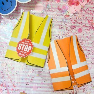 May include: Two paper safety vests, one yellow and one orange, with white reflective stripes. The yellow vest has a stop sign that reads "Just wanted to STOP and say thanks!". The background is pink with confetti and smiley face cutouts.