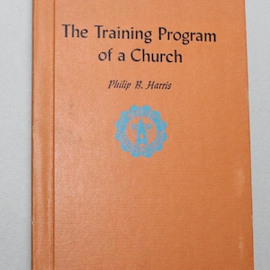 Peut inclure: Livre orange intitulé "The Training Program of a Church" par Philip B. Harris. La couverture présente un texte noir et un emblème bleu et blanc. Le livre semble légèrement usé.