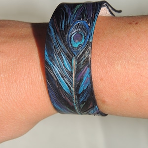 May include: A black leather bracelet with a peacock feather design in shades of blue, teal, and purple.