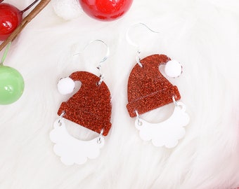 May include: A pair of red glitter Santa hat earrings with white fuzzy trim. The earrings are on a white fluffy surface.