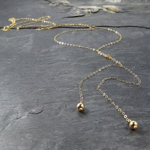 May include: A gold chain necklace with two dangling gold beads at the ends.