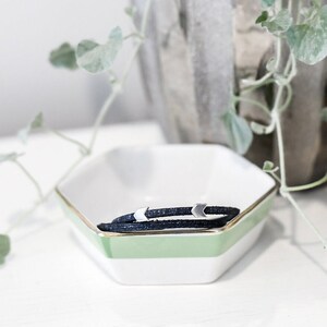 May include: A black leather bracelet with silver arrow charms in a white and green hexagonal dish.