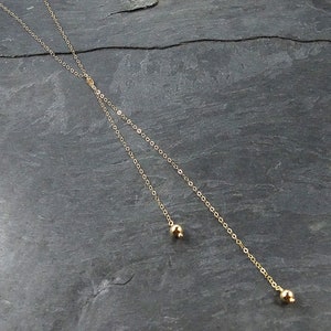 May include: A gold chain necklace with two small gold balls at the ends.