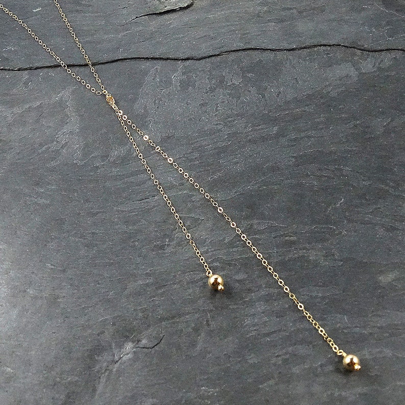 May include: A gold chain necklace with two small gold balls at the ends.