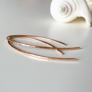 Könnte beinhalten: Ein Paar Ohrringe aus roségoldfarbenem, gehämmertem Draht. Die Ohrringe sind lang und dünn und haben ein zartes, minimalistisches Design.