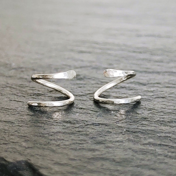 May include: Two silver hammered wire ear cuffs. The cuffs are twisted into a spiral shape.