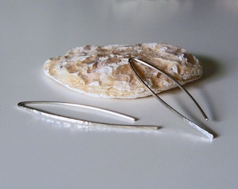 May include: A pair of silver hammered earrings with a long, thin, curved shape.