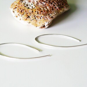 May include: A pair of silver hoop earrings with a thin, curved design. The earrings are simple and elegant.