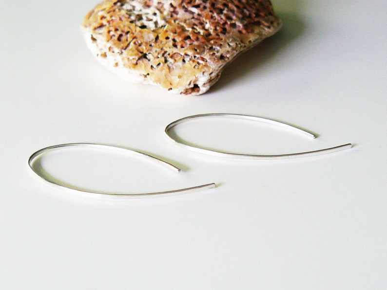 May include: A pair of silver hoop earrings with a thin, curved design. The earrings are simple and elegant.