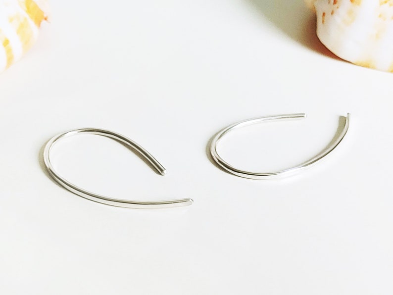 May include: A pair of silver hoop earrings with a simple, curved design. The earrings are made of a thin, smooth metal and have a minimalist aesthetic.