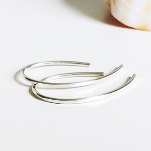 May include: A pair of silver hoop earrings. The earrings are simple and elegant, with a smooth, rounded shape.