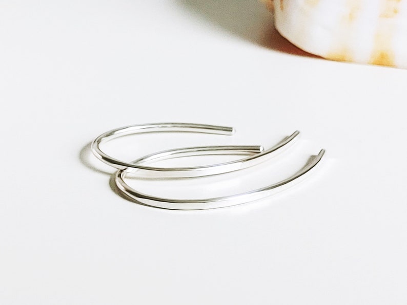 May include: A pair of silver hoop earrings. The earrings are simple and elegant, with a smooth, rounded shape.
