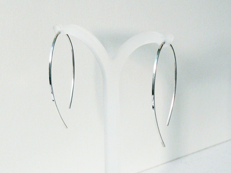 May include: A pair of silver hoop earrings with a hammered finish. The earrings are thin and delicate, and they hang from a simple hook.