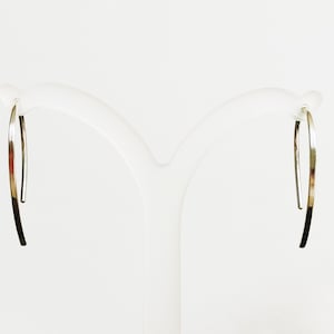 May include: A pair of silver hoop earrings with a simple, curved design. The earrings are displayed on a white stand.
