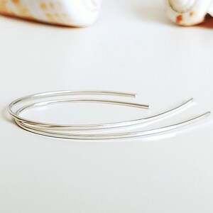 May include: A pair of silver hoop earrings with a simple, minimalist design. The earrings are made of thin, delicate wire and are perfect for everyday wear.