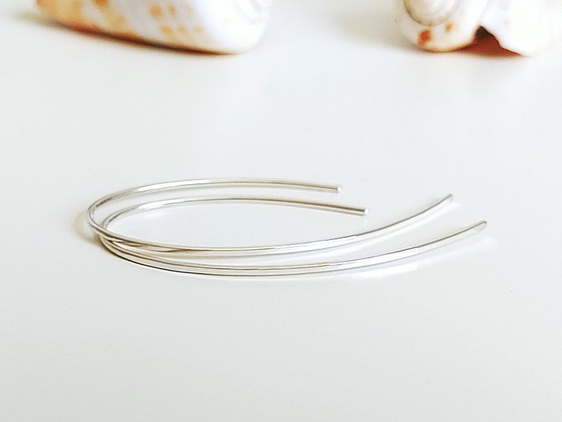 May include: A pair of silver hoop earrings with a simple, minimalist design. The earrings are made of thin, delicate wire and are perfect for everyday wear.