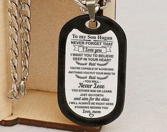 May include: A black dog tag necklace with a silver chain in a wooden box. The dog tag has an inscription that reads "To my Son Hagan NEVER FORGET THAT I Love you I WANT YOU TO BELIEVE DEEP IN YOUR HEART that YOU'RE CAPABLE OF ACHIEVING ANYTHING YOU PUT YOUR MIND TO that -YOU WILL- Never Lose YOU EITHER WIN OR LEARN JUST GO FORTH and aim for the skies I WILL ALWAYS BE RIGHT HERE STANDING BEHIND YOU Love, mom ♡"