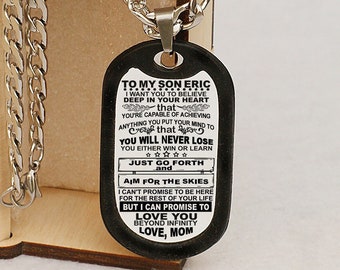 May include: A black dog tag necklace with a silver chain in a wooden box. The dog tag has a message for a son, "To my son Eric, I want you to believe deep in your heart that you're capable of achieving anything you put your mind to. That you will never lose. You either win or learn. Just go forth and aim for the skies. I can't promise to be here for the rest of your life, but I can promise to love you beyond infinity. Love, Mom."