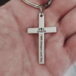 May include: Silver cross keychain with the initials K and J, a heart symbol, and the date 3/18/19 engraved on the top. The words "I Will Always Love You" are engraved on the side of the cross.