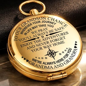 May include: A gold-colored compass with a ring at the top. The compass has engraved text that reads "To our Grandson Chance...We're always here for you Grandma and Grandpa". The compass features a compass rose design.
