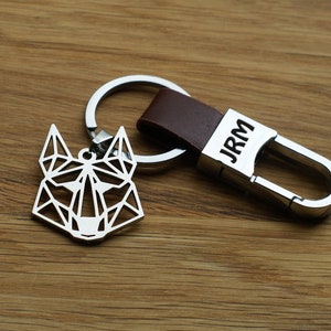 May include: A silver geometric wolf keychain with a brown leather strap and a silver metal clasp. The clasp has the initials "JRM" engraved on it.