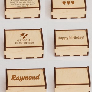 May include: Set of six wooden boxes with engraved text. The boxes are light brown with a dark brown border. The text on the boxes includes "Miguel", "You text here", "S.D.S.U. CLASS OF 2020", "Happy birthday!", "Raymond", and a blank box.