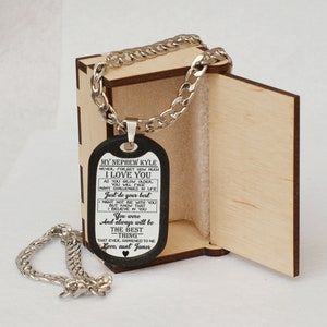 May include: A black dog tag necklace with a silver chain in a wooden box. The dog tag has an inscription that reads "My Nephew Kyle Never forget how much I love you As you grow older you will face many challenges in life Just do your best I might not be with you but know that I believe in you You were and always will be the best -thing- that ever happened to me Love, aunt James"