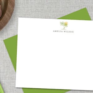 May include: A white card with a green envelope. The card has a simple drawing of a palm tree with a sun above it. The text "Amelia Wilson" is printed below the drawing.