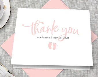May include: A white thank you card with pink lettering and a pink footprint design. The text reads "thank you" with the name "amelia rose" and the date "may 15, 2020" below.