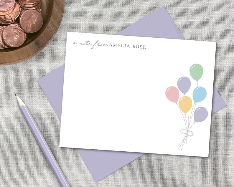 Może przedstawiać: Biała kartka z fioletową kopertą. Na kartce widnieje tekst "a note from AMELIA ROSE" u g&oacute;ry i rysunek wiązki pastelowych balon&oacute;w w prawym dolnym rogu.