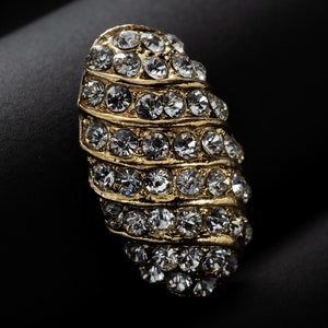 May include: A gold-toned ring with a swirl design set with clear rhinestones.