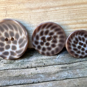 May include: Three brown and white shell buttons with two holes each. The buttons are different sizes and have a swirl pattern.