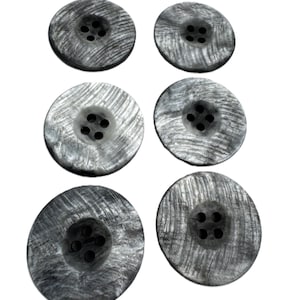 May include: Six round, grey buttons with four holes each. The buttons have a textured, wood-like appearance, with a swirling grain pattern. The buttons are arranged in two rows of three against a white background.