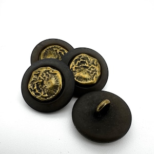 May include: Four dark brown buttons with a textured, antique gold centre. The buttons are round with a shank on the back of one button. The buttons are on a white background.