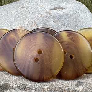 May include: Five round buttons in brown and yellow with two holes each. The buttons have a swirl pattern.