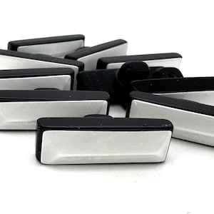 May include: A group of black plastic drawer pulls with a white rectangular insert. The pulls are arranged in a pile.
