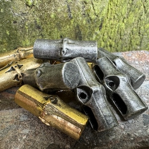 May include: A close-up of a pile of metal and gold bamboo-shaped toggles. The toggles are in various shades of gray and gold, and some have a textured surface.
