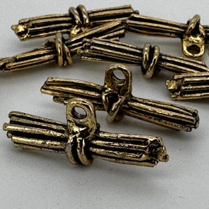 May include: A set of six gold-toned metal buttons shaped like bundles of wheat stalks. The buttons have a hole in the centre for sewing.
