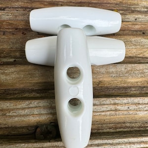 May include: Three white plastic toggle buttons, each with two holes. The buttons are stacked, with the top button lying horizontally and the bottom two buttons lying vertically.