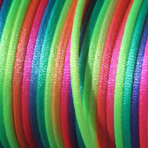 May include: A close-up of a spool of colorful iridescent cord. The cord is arranged in a rainbow pattern with shades of green, blue, pink, orange, and yellow.