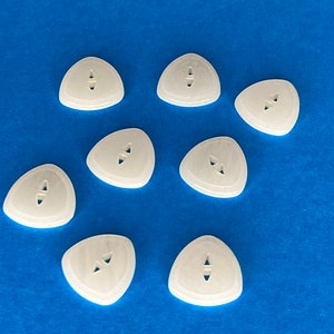 May include: Eight white triangular guitar picks with a small hole in the center. The picks are arranged in a circle on a blue background.