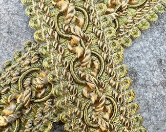 May include: A close-up of a green and gold braided trim with a decorative pattern. The trim is made of a soft, flexible material and has a subtle sheen.