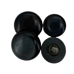May include: Four black, round buttons with a glossy finish. One button has a visible shank on the back. The buttons are arranged in a cluster against a white background.