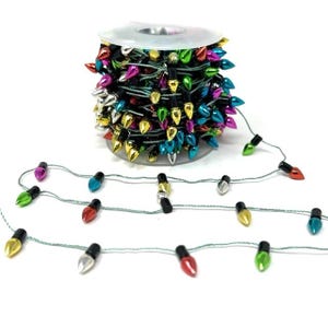 Könnte beinhalten: Eine Rolle bunter Weihnachtsbeleuchtung mit einer Vielzahl von Juwelenfarben, darunter Rot, Grün, Blau, Silber und Gold. Die Lichter sind auf einem grünen Draht aufgereiht, wobei einige Lichter vor der Rolle ausgebreitet sind.