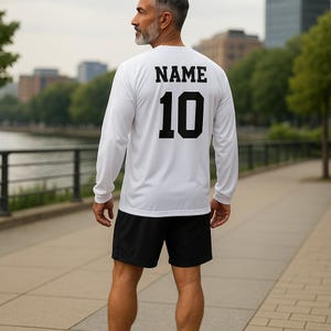 K&ouml;nnte beinhalten: Wei&szlig;es Langarm-Trikot mit schwarzem Text auf der R&uuml;ckseite, der "NAME 10" lautet.