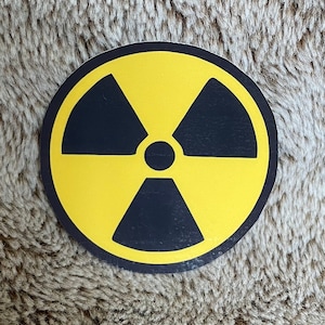 May include: A circular yellow and black radiation symbol. The symbol has a yellow circle with a black centre and three black blades. The symbol is set against a brown, textured background.
