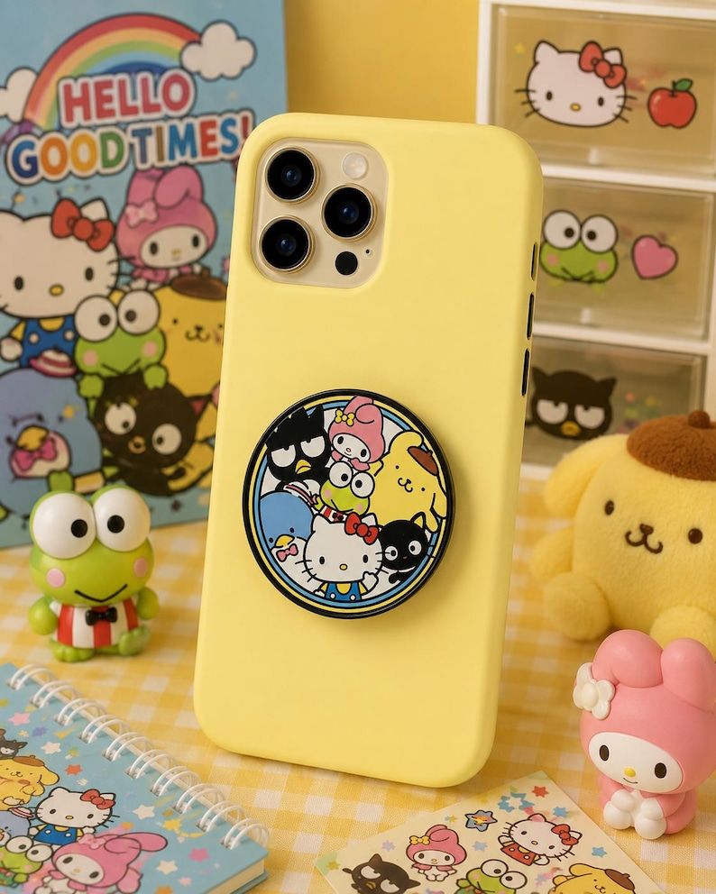Może przedstawiać: Jasnoż&oacute;łte etui na smartfona z okrągłym, składanym uchwytem z tyłu. Uchwyt przedstawia kolorową grafikę r&oacute;żnych postaci Sanrio, w tym Hello Kitty, My Melody, Keroppi, Pompompurin, Badtz-Maru oraz Tuxedosam.
