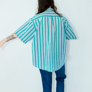 Puede incluir: Una camisa de botones a rayas con rayas verdes y blancas. La camisa es de gran tama&ntilde;o y tiene mangas cortas.