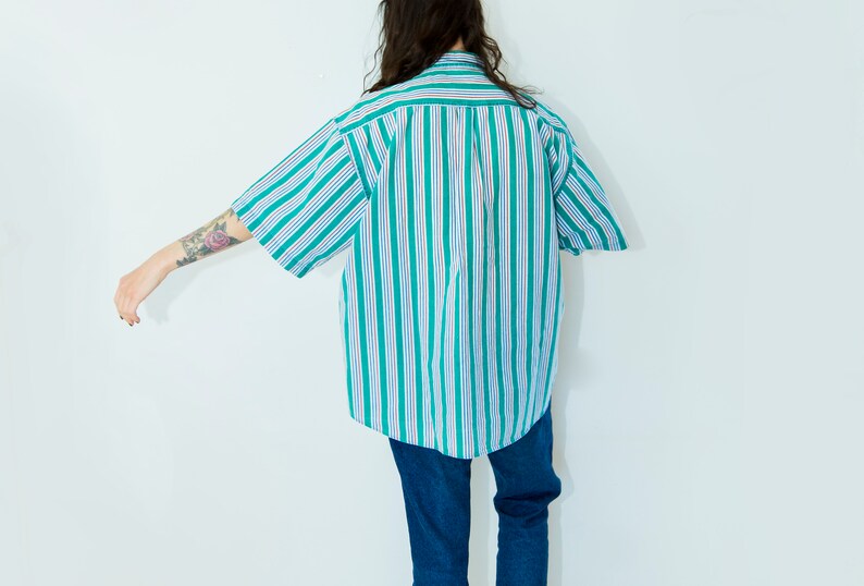 Puede incluir: Una camisa de botones a rayas con rayas verdes y blancas. La camisa es de gran tama&ntilde;o y tiene mangas cortas.